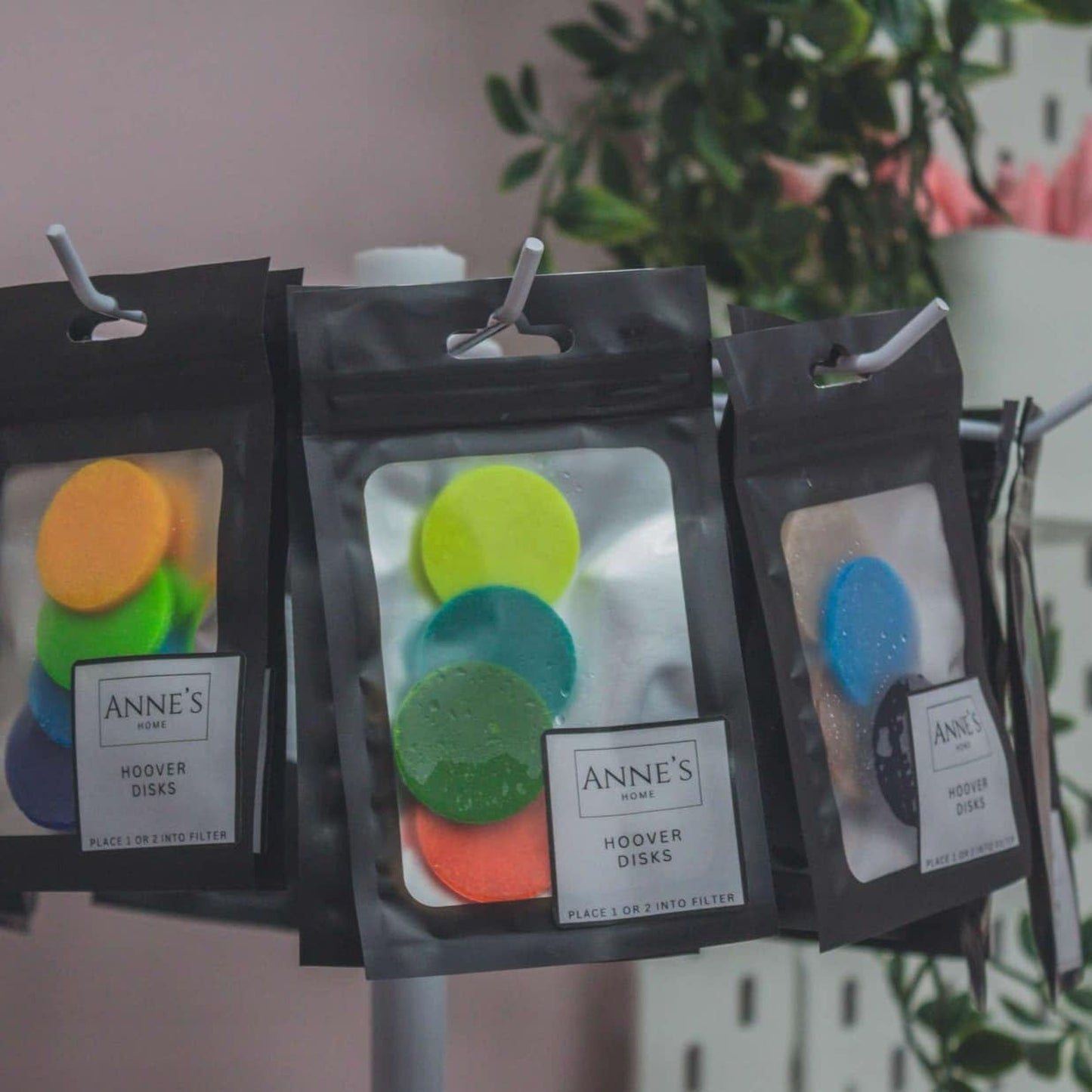 three packages of colorful plastic disks hanging from a hook, with a plant visible in the background.